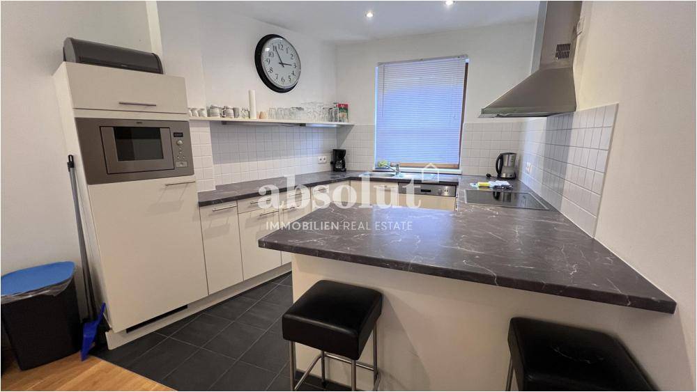 Moderne Küche mit Frühstücksbar, dunklen Arbeitsplatten und Fliesenboden.