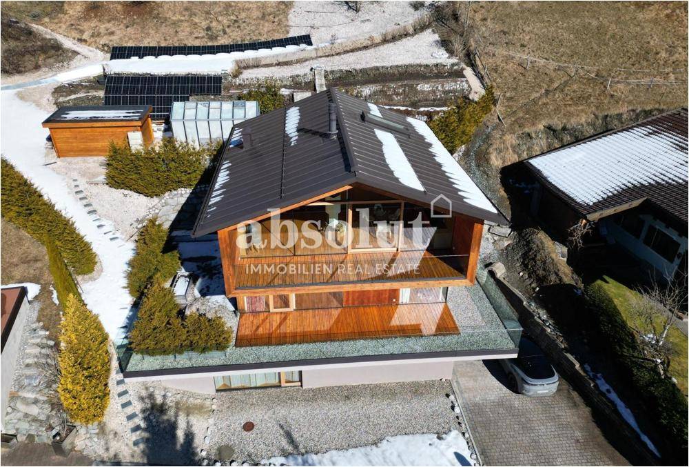 Luftaufnahme eines modernen Holzhauses mit Solaranlage auf dem Dach in verschneiter Landschaft.