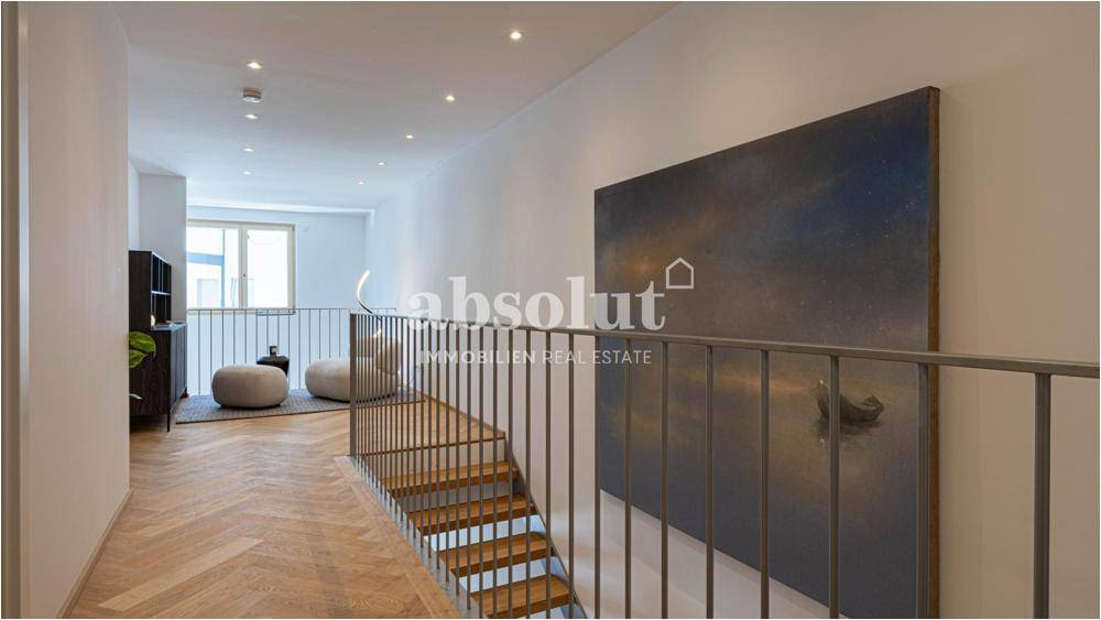 Heller Flur mit eleganter Treppe, Fischgrätparkett und moderner Kunst an der Wand.
