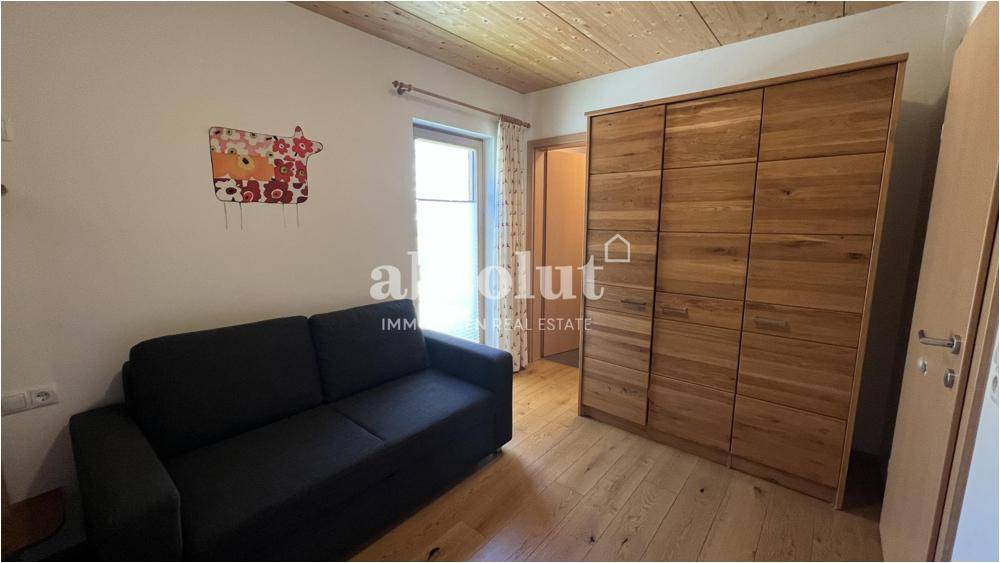 Schlafzimmer mit Holzboden, großem Holzschrank und Zugang zu einem Fenster.