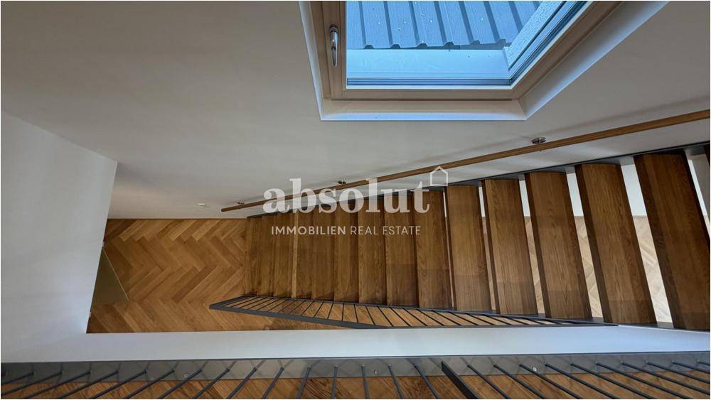 Treppenhaus mit Holzstufen, Fischgrätparkett und Oberlicht für natürliches Licht.