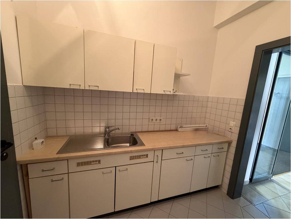 Kleine, funktionale Küchenzeile mit weißen Schränken, Edelstahlspüle und gefliestem Spritzschutz.