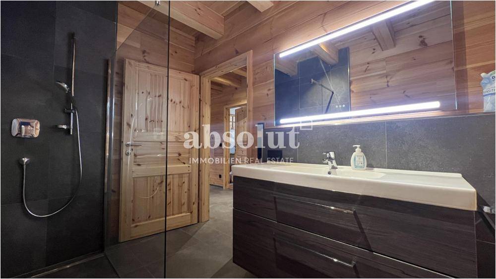 Modernes Badezimmer mit dunklen Fliesen, Einzelwaschbecken und großer begehbarer Dusche.