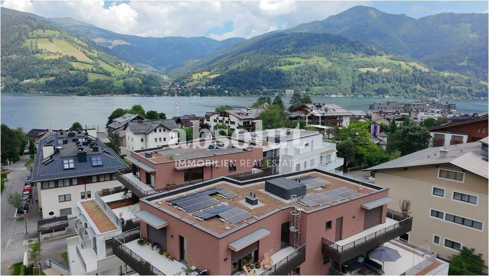 Luftaufnahme eines modernen Wohngebäudes mit Solaranlage und Seeblick in bergiger Landschaft.