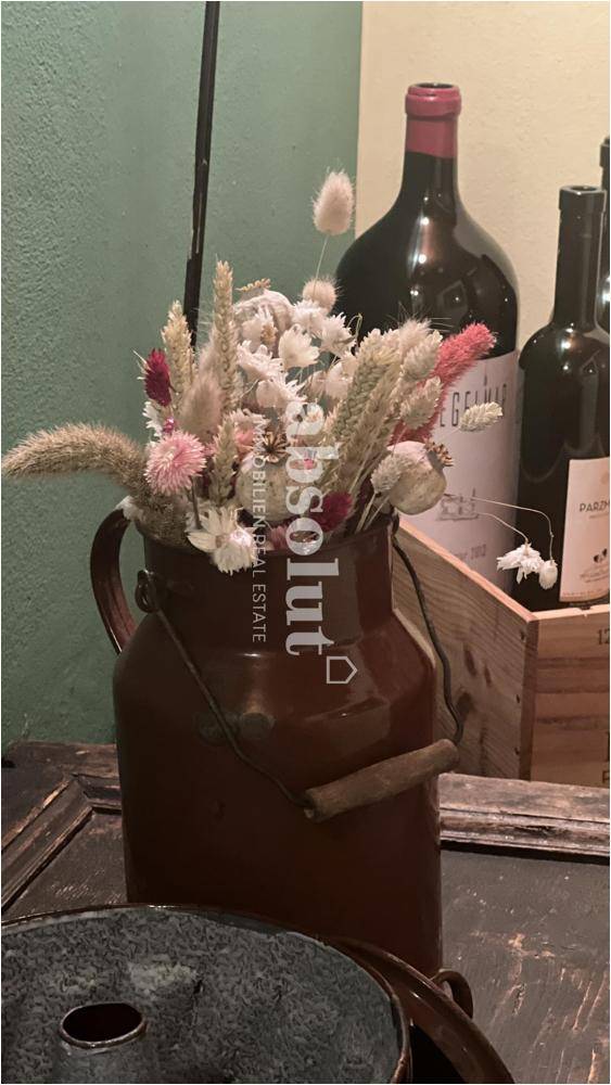 Dekorative Blumenarrangements in einem rustikalen Gefäß auf einem Holztisch, umgeben von Weinflaschen.