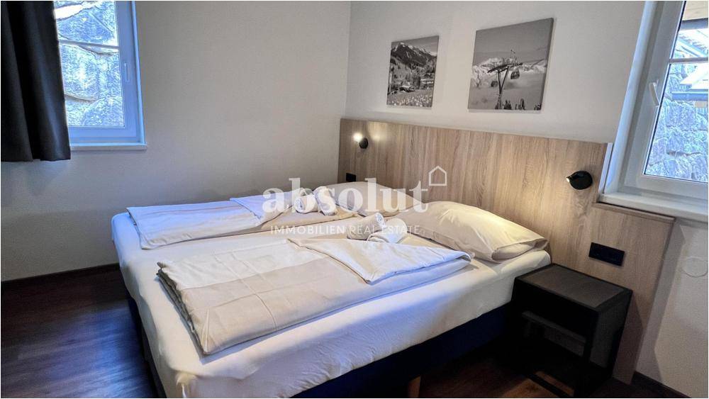 Schlafzimmer mit Doppelbett, Holzkopfteil und zwei Fenstern für natürliches Licht.