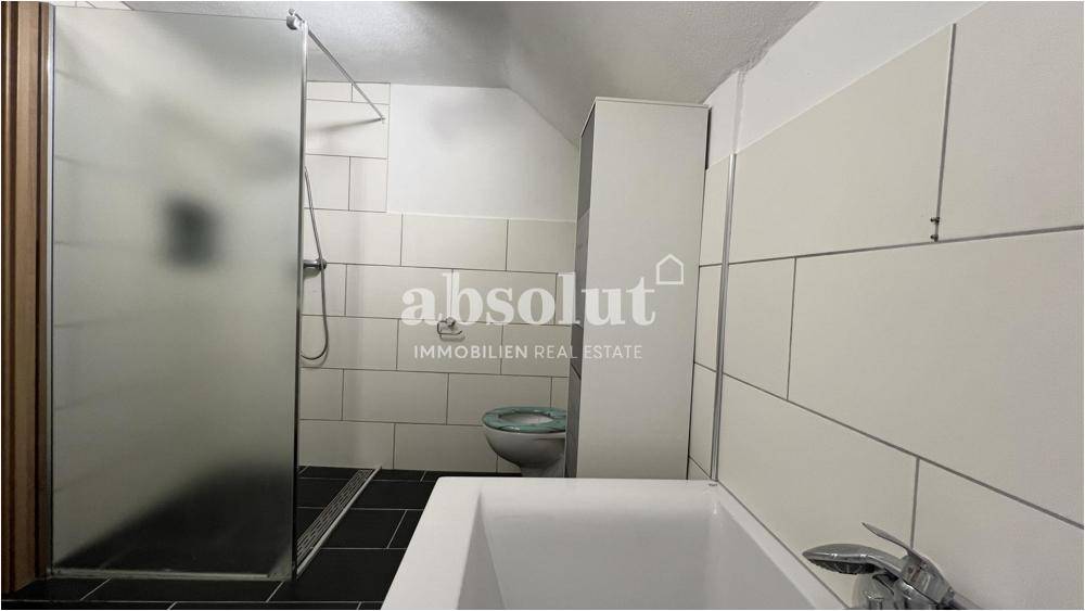 Badezimmer mit Duschkabine, Toilette und weißen Wandfliesen.
