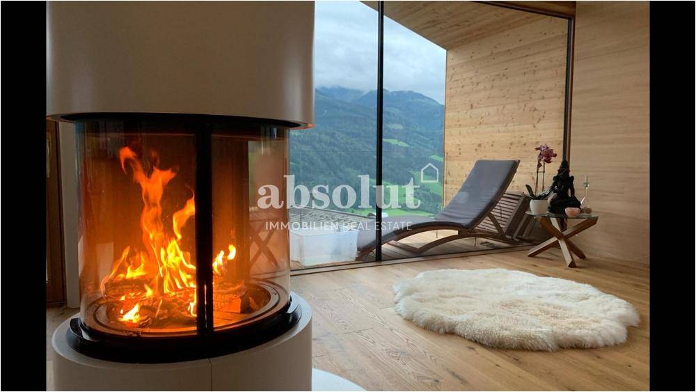 Gemütlicher Wohnbereich mit Kamin, Holzboden und Liegestühlen vor der Bergkulisse.