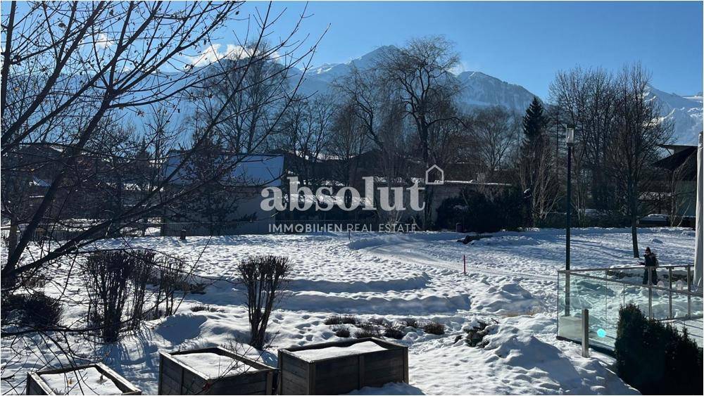 Winterliche Landschaft mit schneebedecktem Garten und beeindruckendem Bergblick von einer Terrasse.