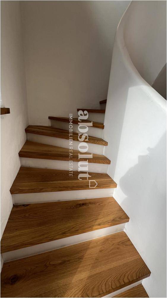 Elegante Holztreppe mit weiß gestrichenen Stufen in einem hellen Treppenhaus.