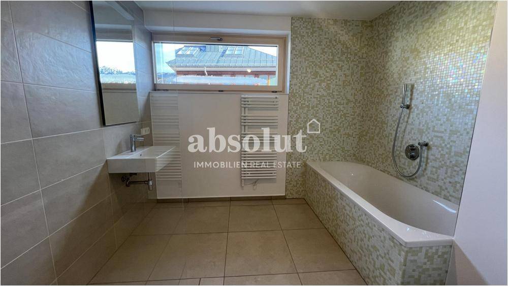 Modernes Badezimmer mit Badewanne, Fliesenboden und Fenster, ausgestattet mit einem Handtuchheizkörper.