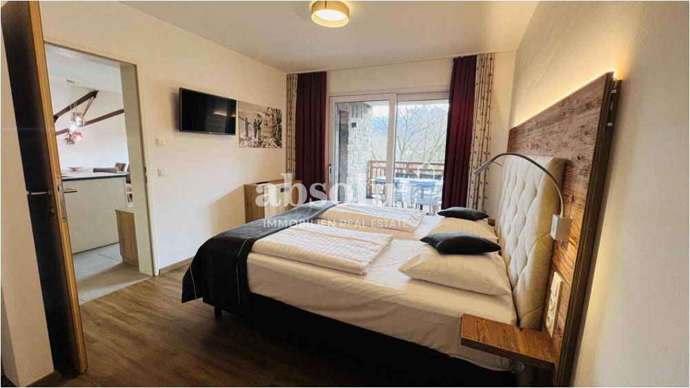 Geräumiges Schlafzimmer mit Holzboden, TV und Balkonzugang mit Bergblick.