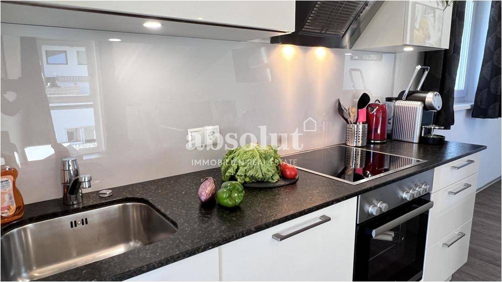 Moderne Einbauküche mit dunkler Granitarbeitsplatte, Induktionskochfeld und integriertem Backofen.