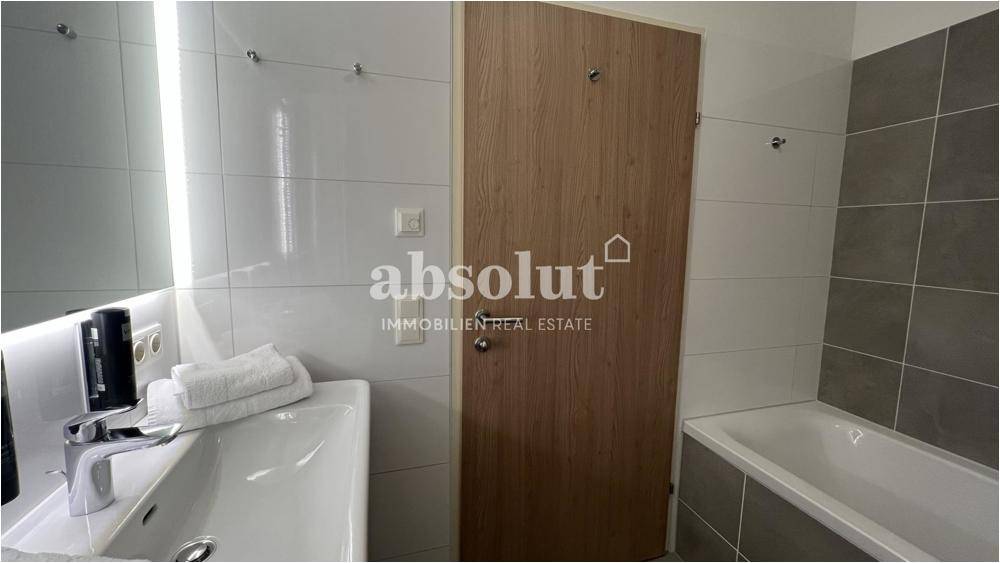 Helles Badezimmer mit Badewanne, Einzelwaschbecken und modernen Fliesen.