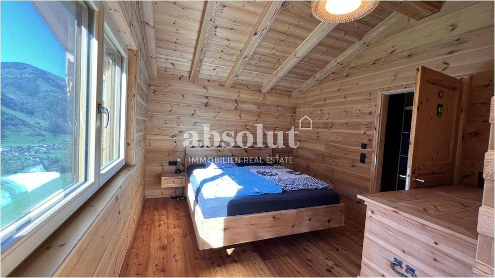 Gemütliches Schlafzimmer mit Holzwänden, Holzboden und großem Fenster mit Bergblick.