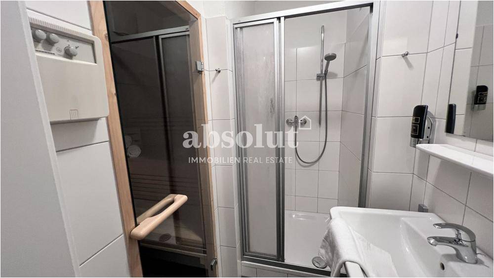 Badezimmer mit Duschkabine, Waschbecken und Zugang zu einer privaten Sauna für Wellnessmomente.