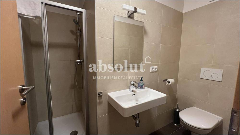 Modernes Badezimmer mit Duschkabine, Waschbecken und Wand-WC, hell gefliest.