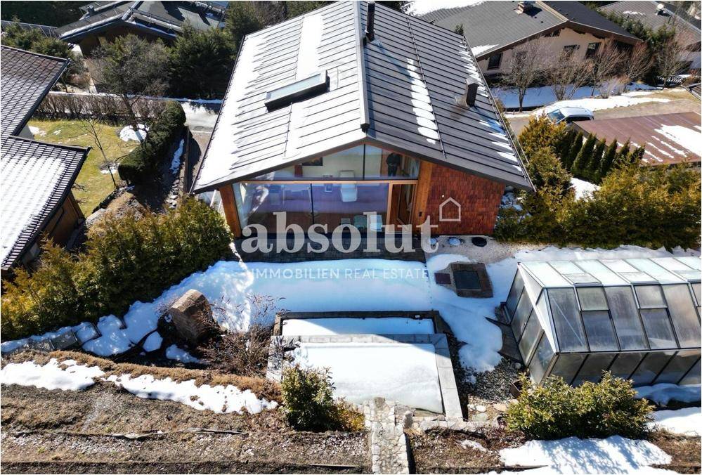 Luftaufnahme eines modernen Hauses mit Glasfronten, umgeben von Schnee und einem Gewächshaus.