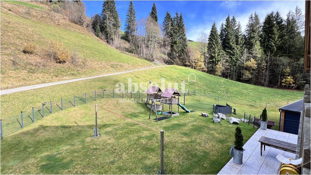 Gepflegter Garten mit Rasenfläche, Kinderspielplatz und Blick auf die umliegende Natur.