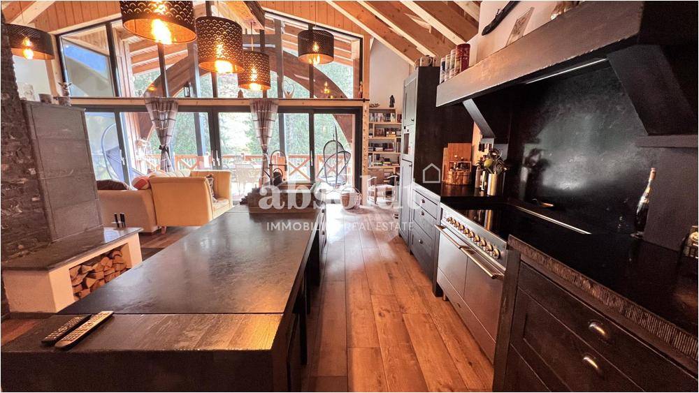Offene Küche mit Holzboden und Blick auf den Wohnbereich mit großen Fenstern und Bergblick.