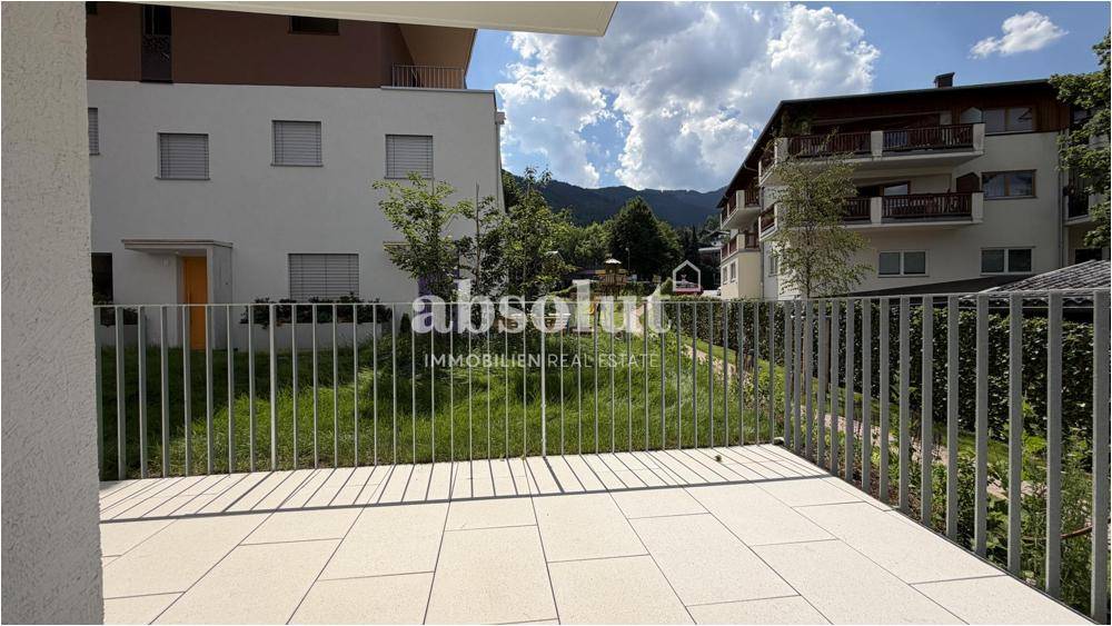 Heller Balkon mit Fliesenboden und Blick auf die umliegenden Gebäude und grüne Hügel.