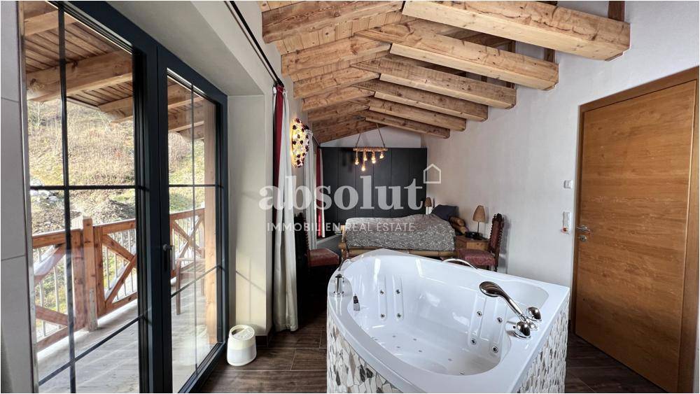 Schlafzimmer mit freistehendem Whirlpool, Holzbalken und Zugang zum Balkon.