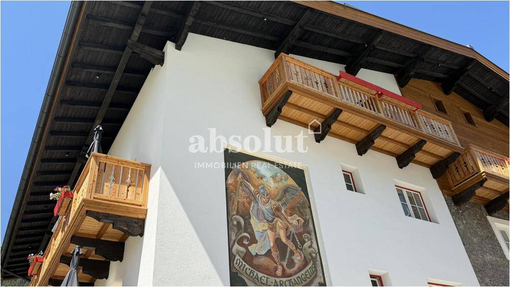 Fassade eines Gebäudes mit einem großen Wandgemälde und traditionellen Holzbalkonen.