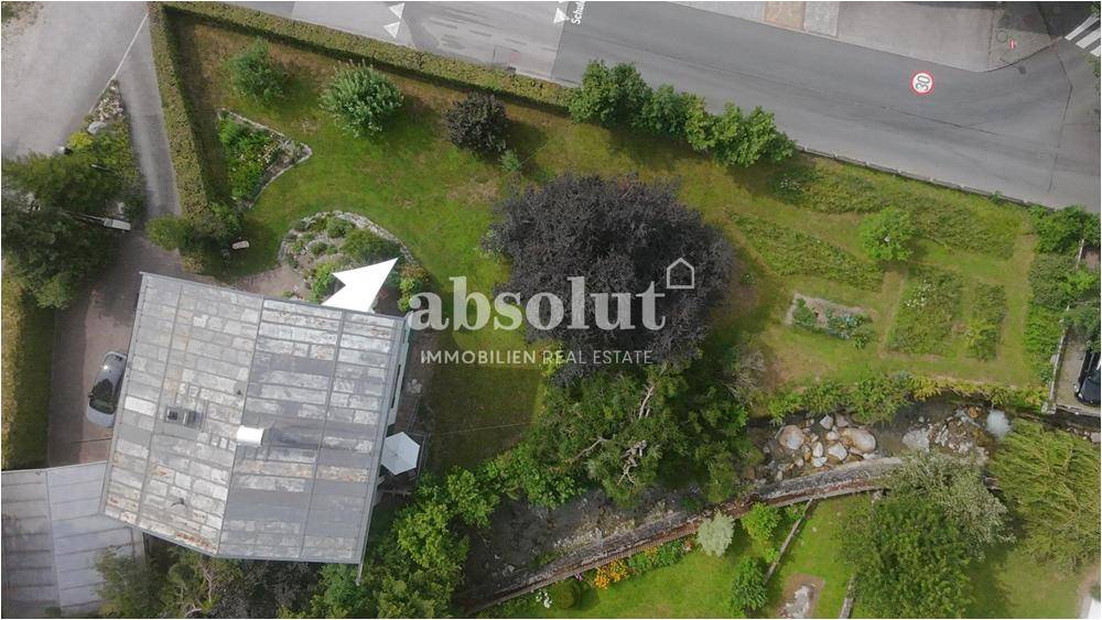 Luftaufnahme des Anwesens mit Haus, großem Garten und angrenzender Straße.