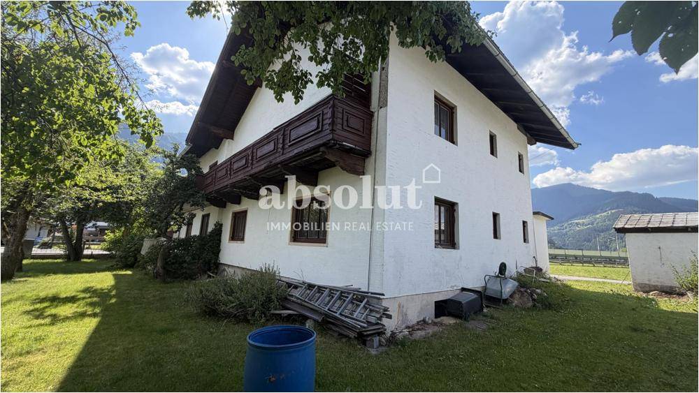 Seitenansicht eines traditionellen Hauses mit Holzbalkon und Gartenbereich unter blauem Himmel.