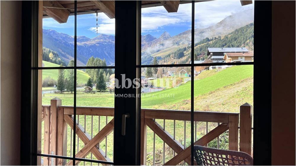 Blick aus dem Fenster auf die umliegende Berglandschaft und einen Holzbalkon.