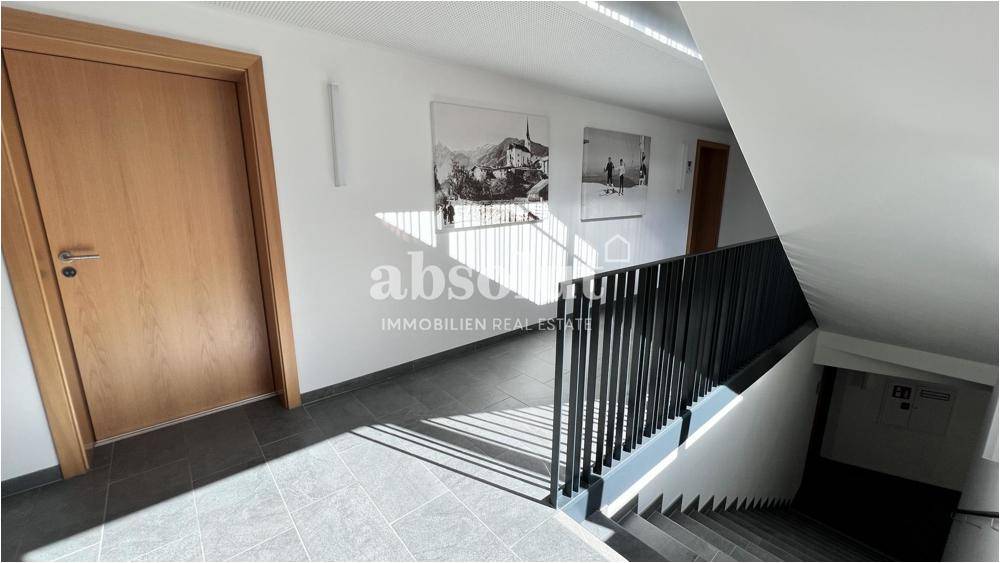 Heller Flur mit Treppenaufgang, modernen Wandbildern und Fliesenboden.