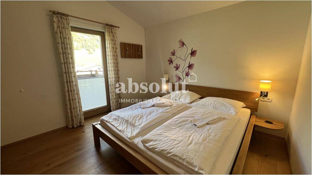Helles Schlafzimmer mit Doppelbett, Holzboden und Zugang zu einem Balkon.