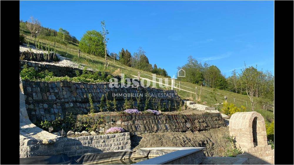 Terrassierter Gartenbereich mit Steinmauern, Bepflanzung und Blick auf die grüne Hügellandschaft.