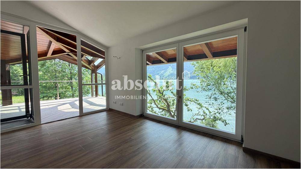 Schlafzimmer mit großen Fenstern, Seeblick und Zugang zu einer überdachten Terrasse, unmöbliert.