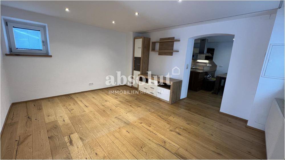 Helles Wohnzimmer mit Holzboden und offenem Zugang zu einem angrenzenden Küchenbereich.