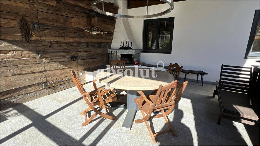 Überdachte Loggia mit rustikalem Holztisch, Stühlen und einem traditionellen Steinkamin für gemütliche Abende.