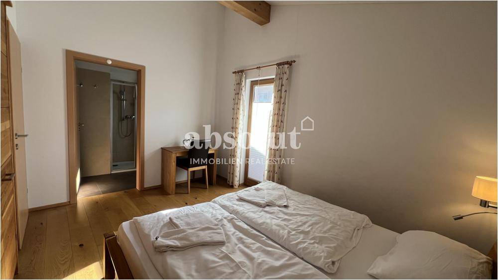 Schlafzimmer mit Doppelbett, Holzboden und direktem Zugang zum Badezimmer.