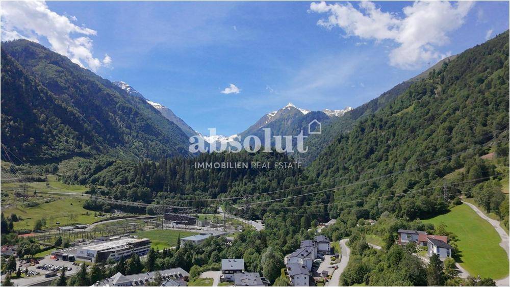 Weitläufige Ansicht eines Tals mit bewaldeten Bergen, Infrastruktur und einem klaren blauen Himmel