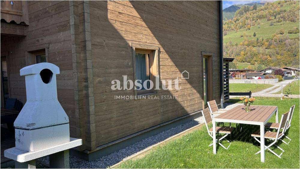 Gartenbereich mit Grill, Esstisch und Rasenfläche neben dem Holzhaus.