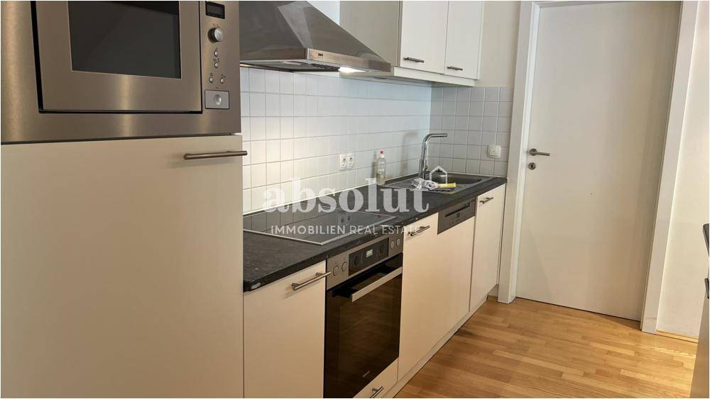 Kompakte, moderne Küche mit weißen Schränken, integrierten Geräten und Holzboden.