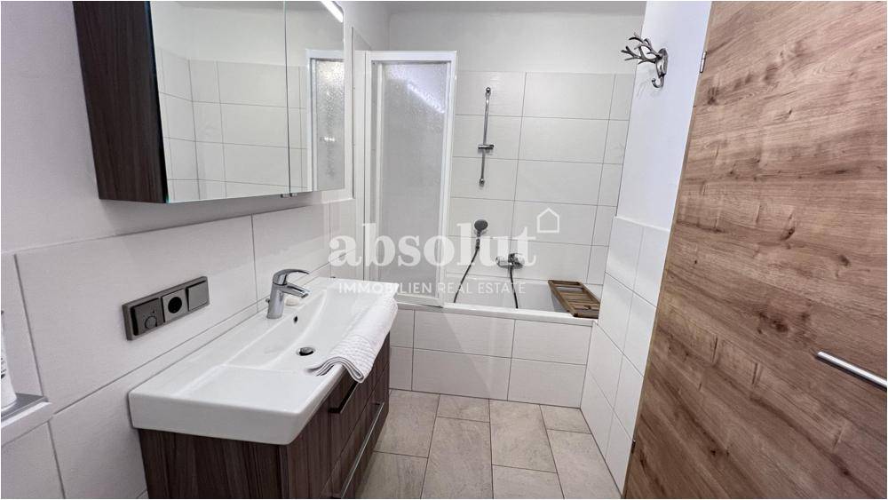 Funktionales Badezimmer mit Badewanne, Waschbecken und Spiegelschrank, hell gefliest.