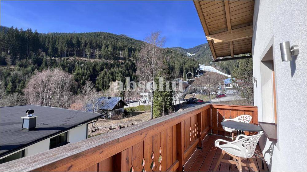 Balkon mit Holzboden und Sitzgelegenheiten, bietet einen weiten Blick auf die Skipiste und Berge.