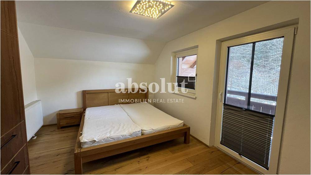 Geräumiges Schlafzimmer mit Holzbett, Holzboden und Balkonzugang.