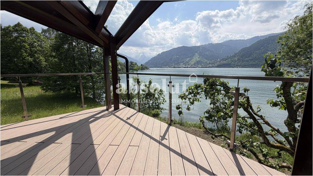 Geräumige überdachte Terrasse mit Seeblick und Glasgeländer, umgeben von Natur und Bergen.