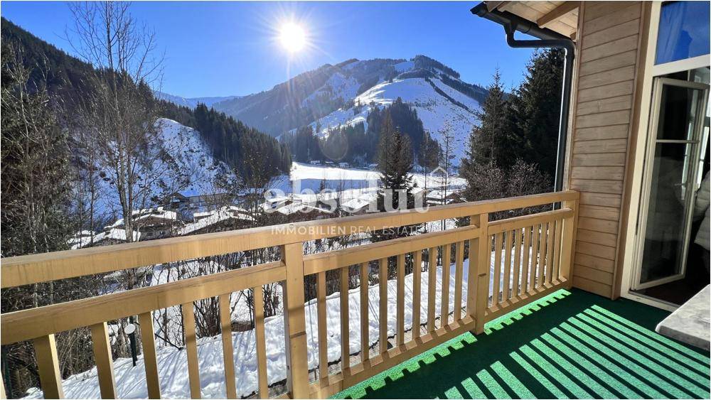 Sonniger Balkon mit Holzbalkongeländer und weitem Blick auf die verschneiten Berge.
