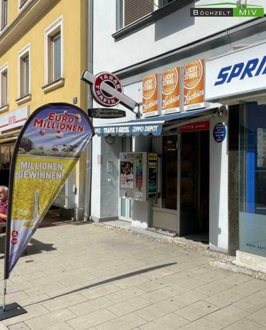 Geschäftsfassade an einer belebten Straße mit Werbeflagge und Markise über dem Eingangsbereich.