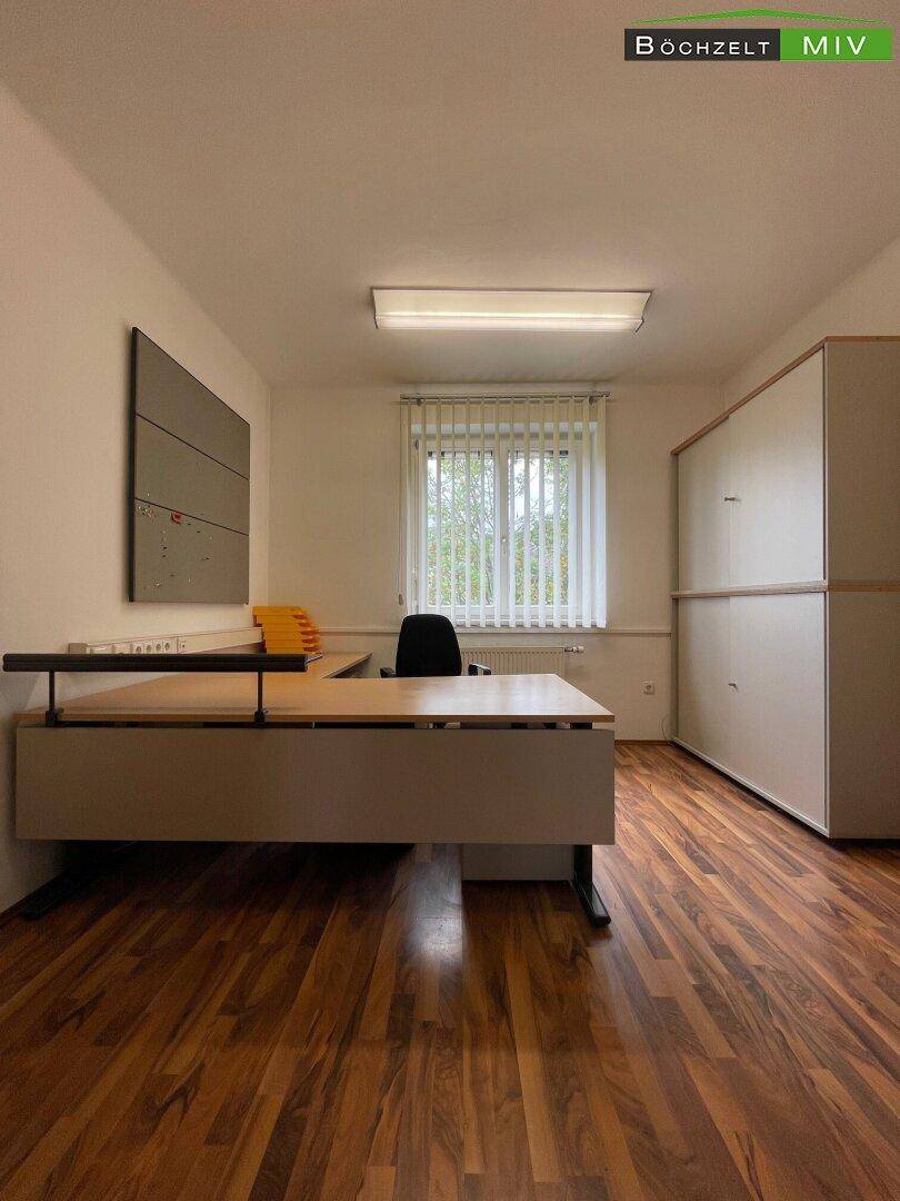 Büroraum mit Holzboden, einem großen Schreibtisch und integrierten Schränken an der Wand für Stauraum.