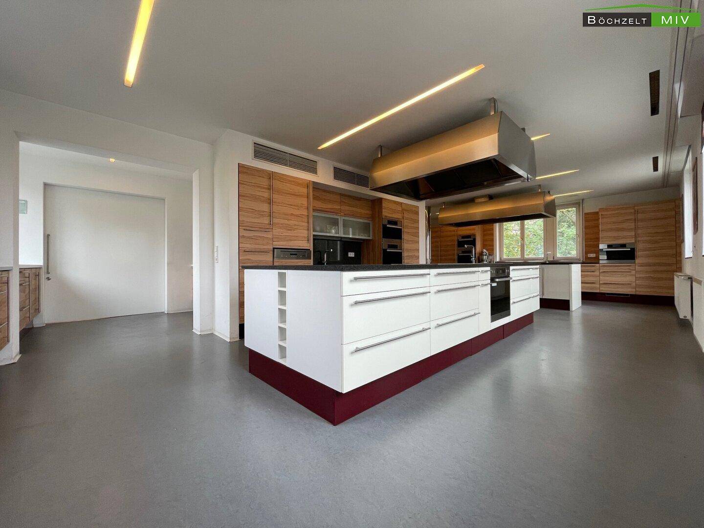 Große, moderne Küche mit zentraler Kochinsel, Holzschränken und professioneller Dunstabzugshaube.