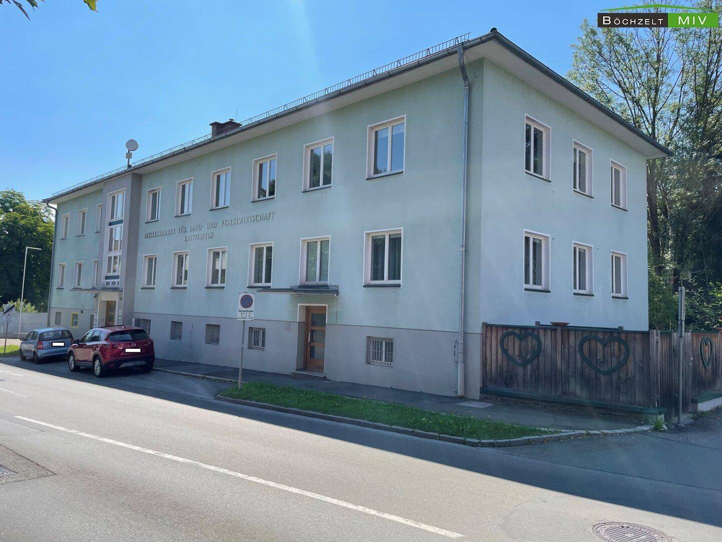 Seitenansicht des Gebäudes mit hellgrüner Fassade, Fenstern und einem Holzzaun mit Herzmotiven.