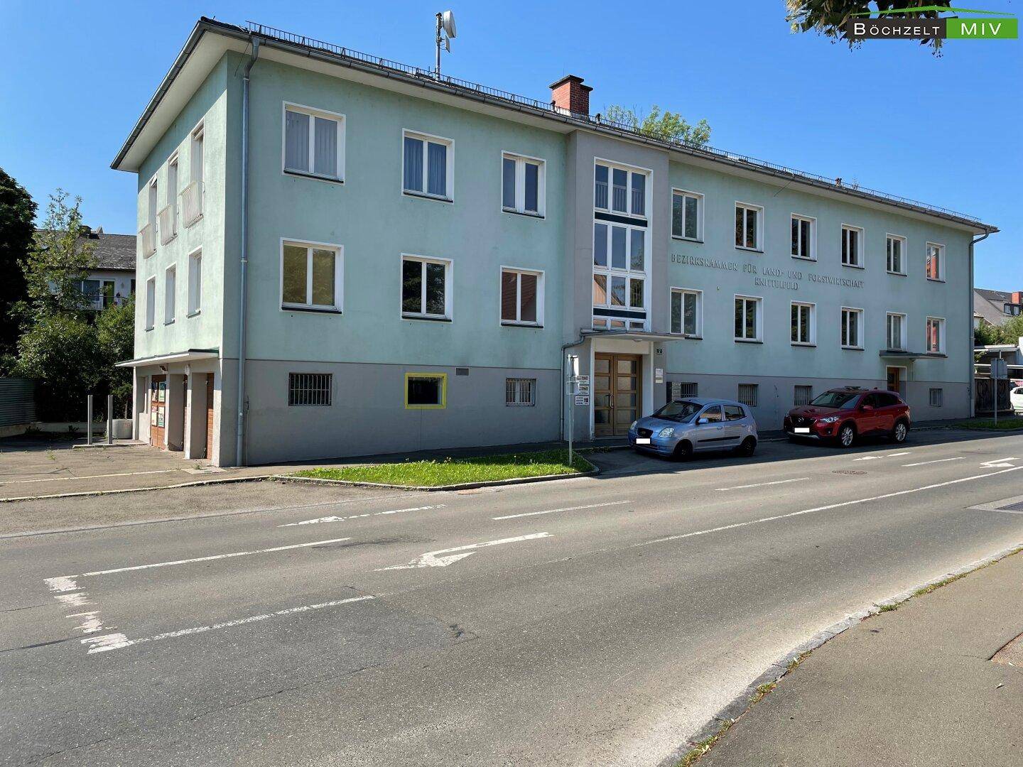 Gebäudeansicht von der Straße mit hellgrüner Fassade und mehreren Fenstern, davor parken zwei Autos.